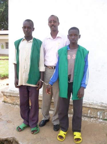 Janvier Ncamatwi (in the middle) with Eric Nimbona (on the right), a child accused of rape with another defendant. The two prisoners are attached by handcuffs.
